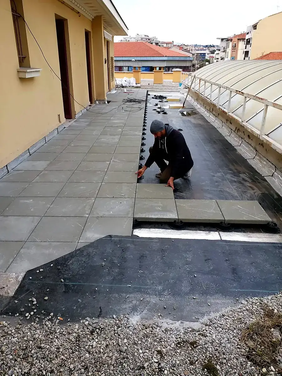 Un compagnon pose des dalles sur plots sur une terrasse