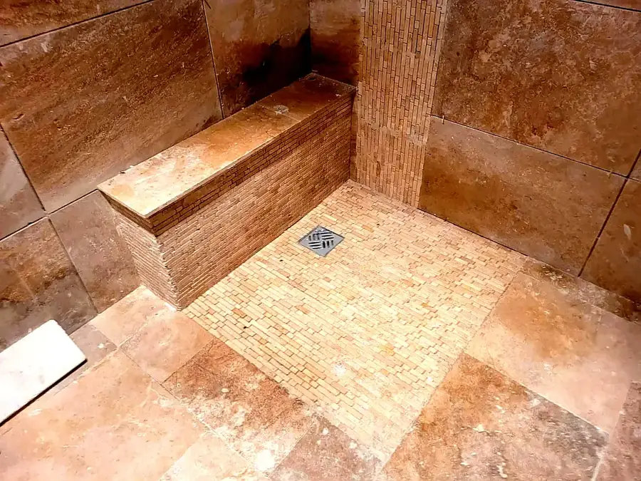 Douche à l'italienne en travertin avec banc maçonné et siphon de sol