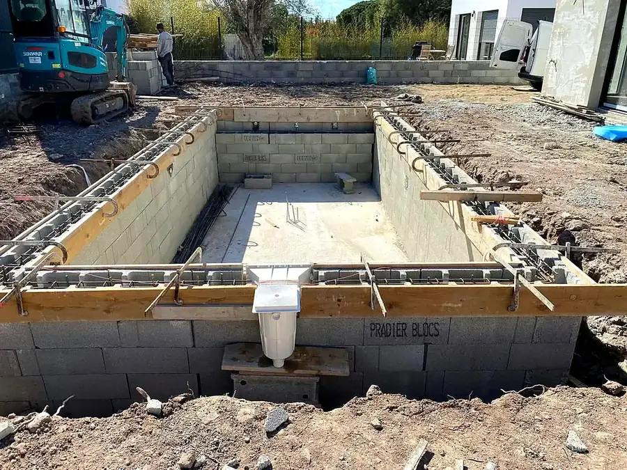 Bassin de piscine monté en blocs, skimmer en place, pelleteuse en arrière-plan